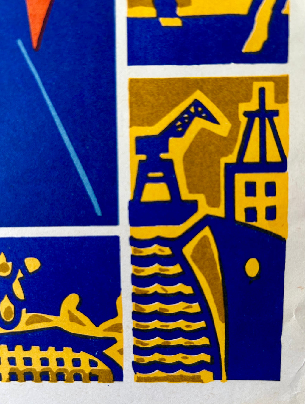 A close-up of a block-print style artwork with bold blue and mustard yellow geometric and architectural shapes, including a crane, buildings, and wavy lines.