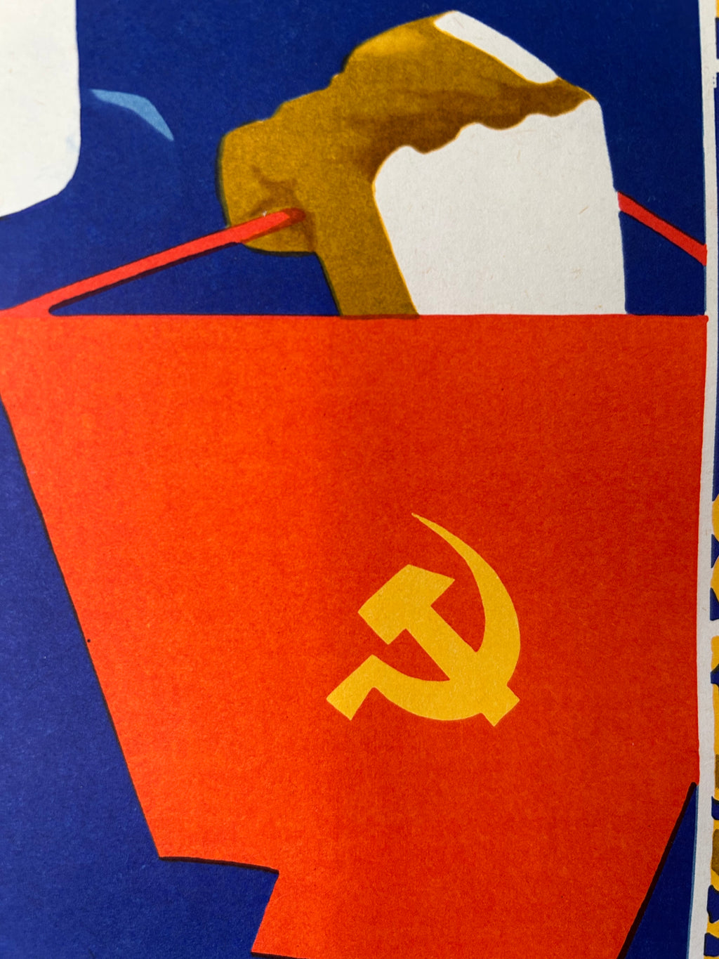 A close-up of a Soviet hammer and sickle symbol printed on a red paper bag or envelope, with a brown and white paper airplane sticking out from the top against a blue background.