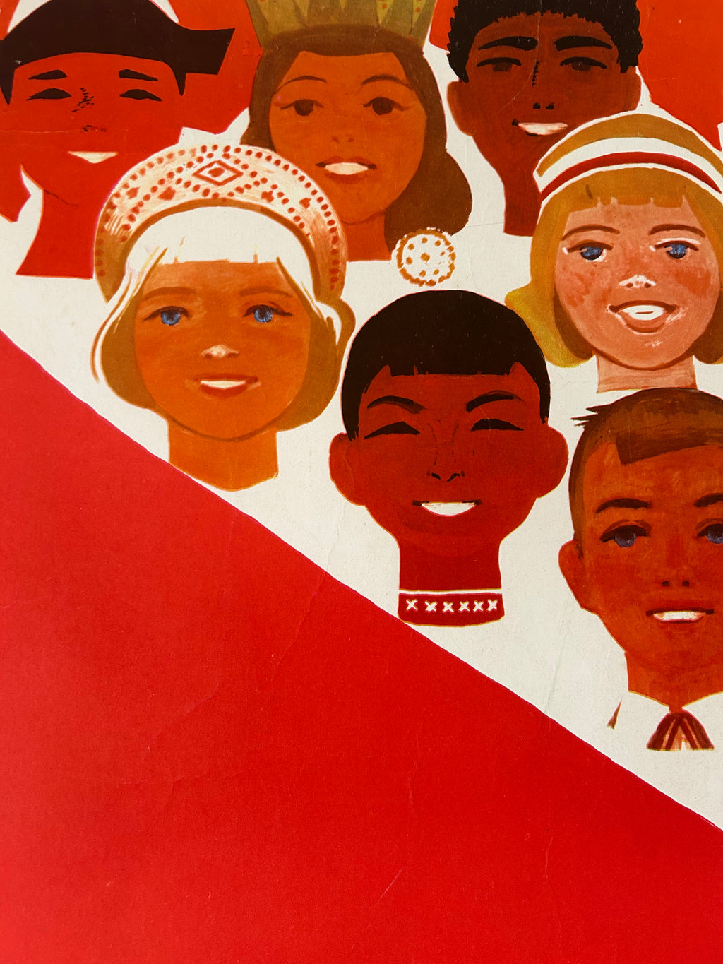 A stylized graphic print featuring multiple illustrated faces of children and adults arranged above a large red diagonal shape on a white background.
