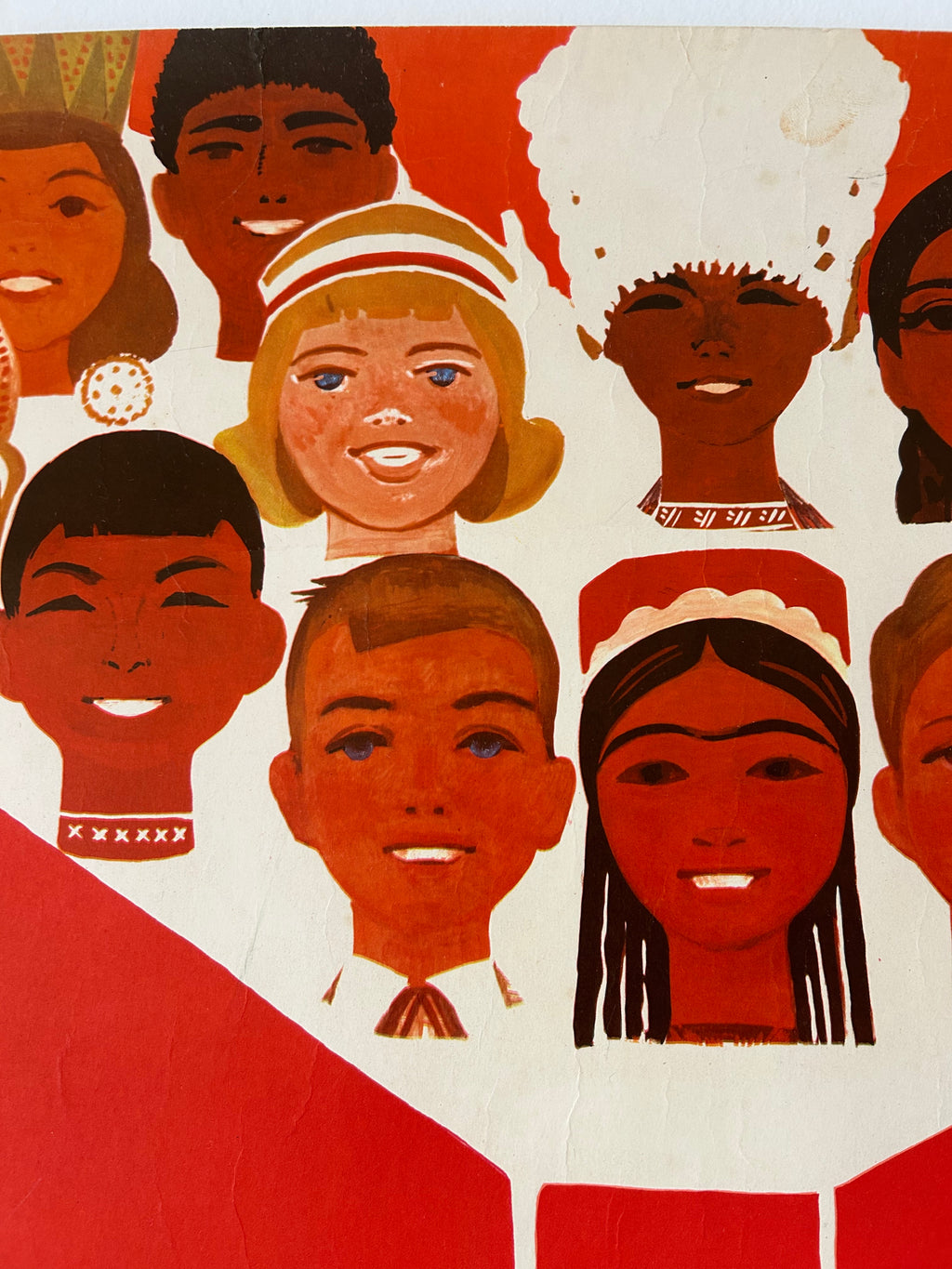 A stylized collage print of illustrated children's faces in warm red, orange, brown, cream, and black tones, with large red geometric shapes at the bottom.