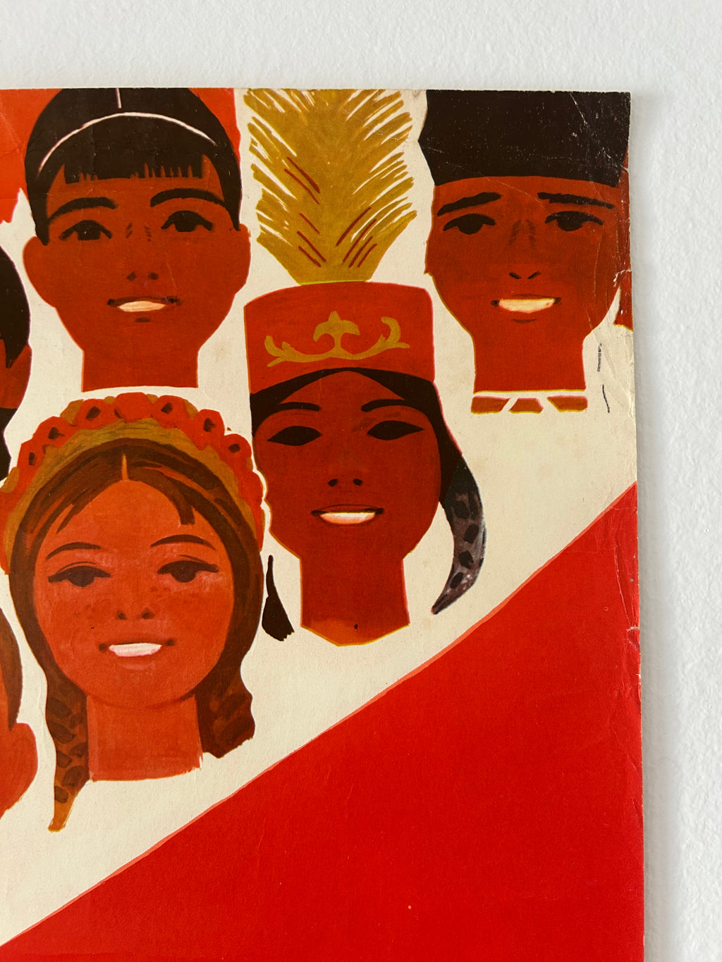 A close-up of a vintage-style illustrated print or poster showing stylized faces in warm red, orange, cream, and black tones, with a bold red diagonal shape across the lower right.