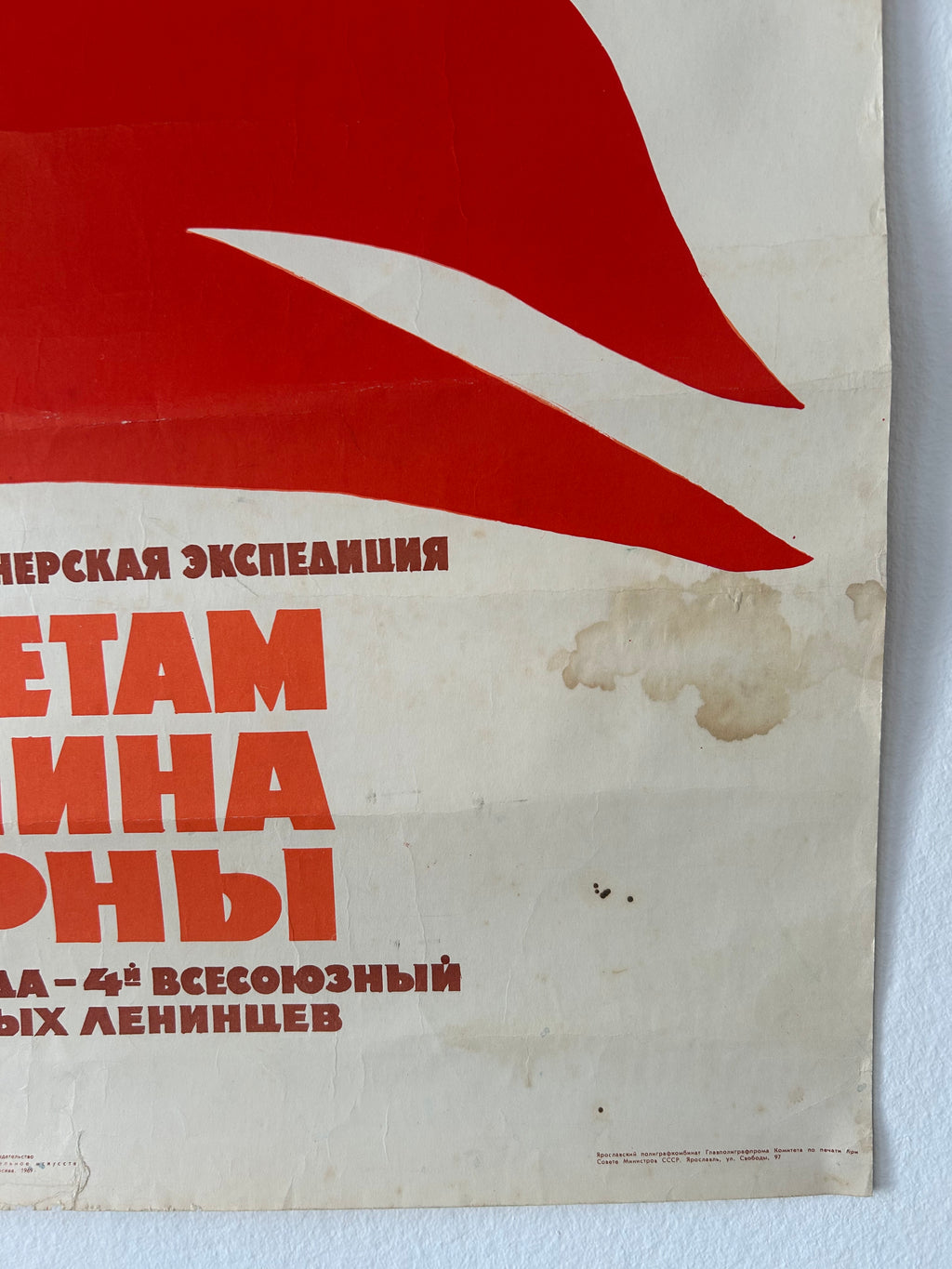 Vintage Soviet-style poster print with a large red abstract shape and bold red Cyrillic text on an off-white background, photographed against a light wall.