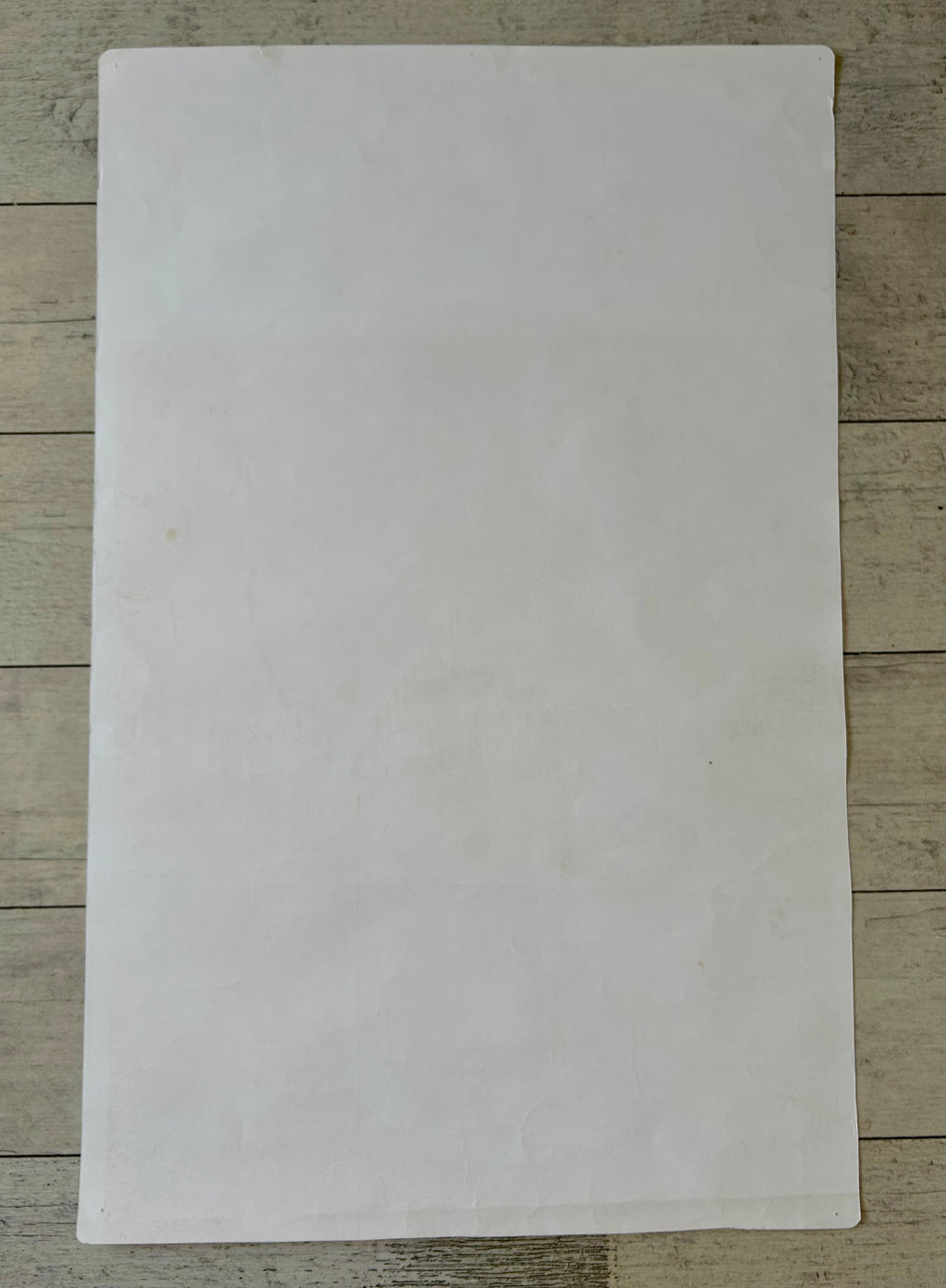 A blank, off-white sheet of paper or cardstock laid flat on a light-colored wooden surface.