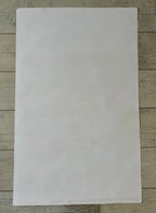 A blank, off-white sheet of paper or cardstock laid flat on a light-colored wooden surface.