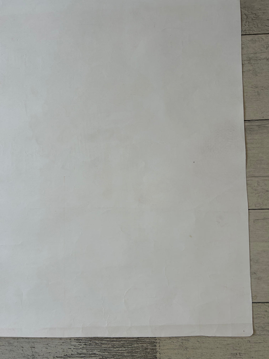 A large, blank white sheet of paper or cardstock laid flat on a light gray wood plank surface.