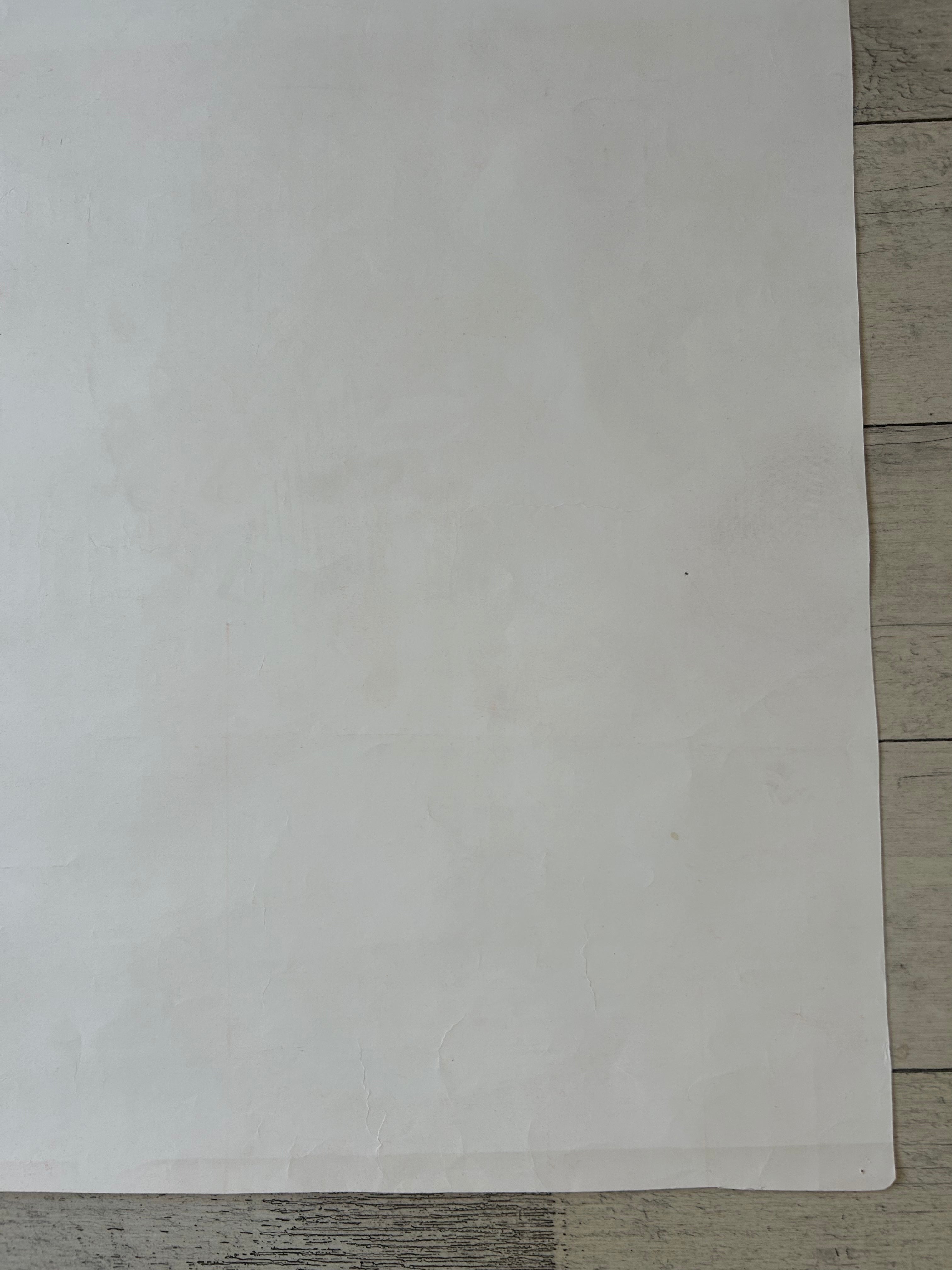 A large, blank white sheet of paper or cardstock laid flat on a light gray wood plank surface.