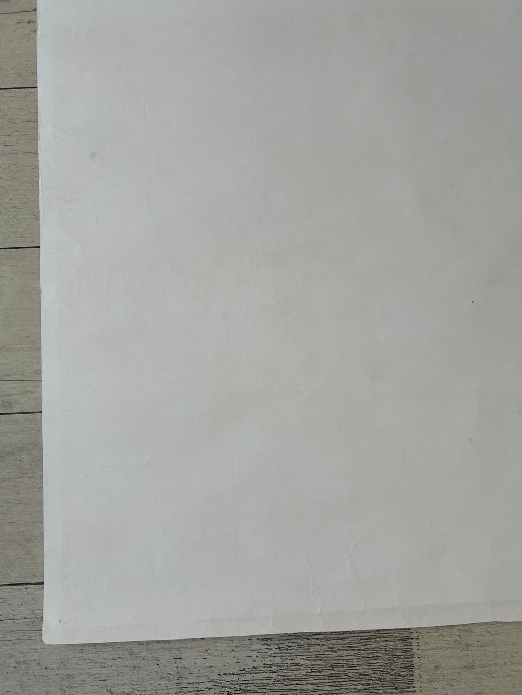 A blank white sheet of paper or cardstock placed on a light gray wood-grain surface.