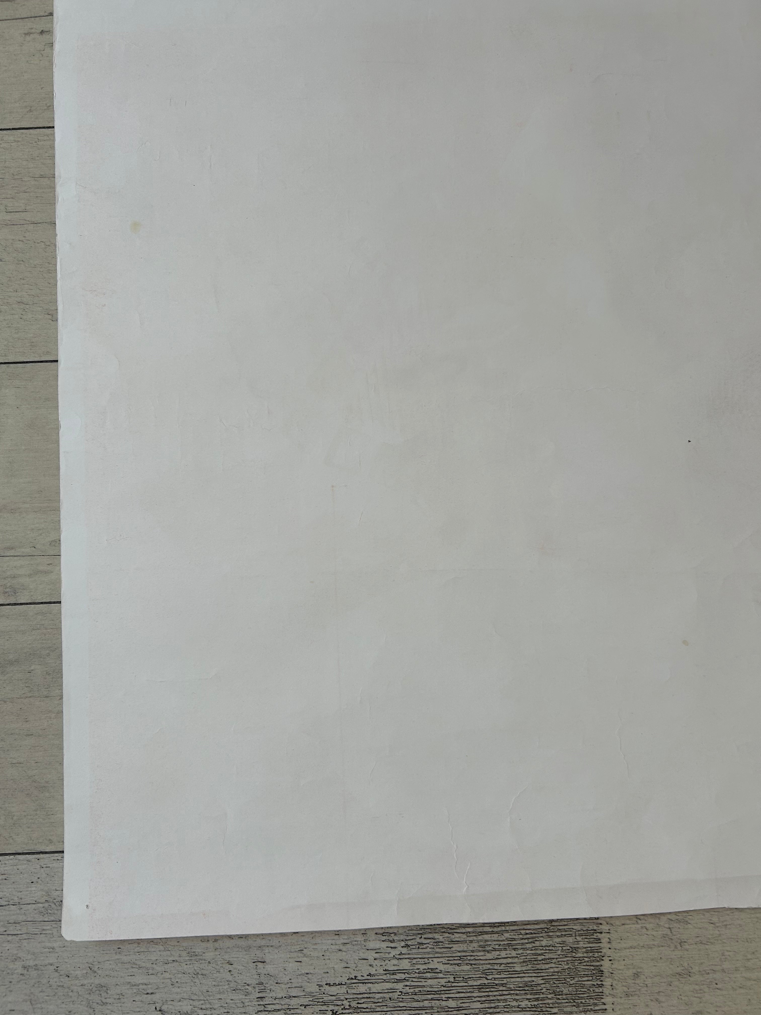 A blank white sheet of paper or cardstock placed on a light gray wood-grain surface.
