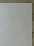 A plain white rectangular sheet or mat laid flat on a light wood surface.