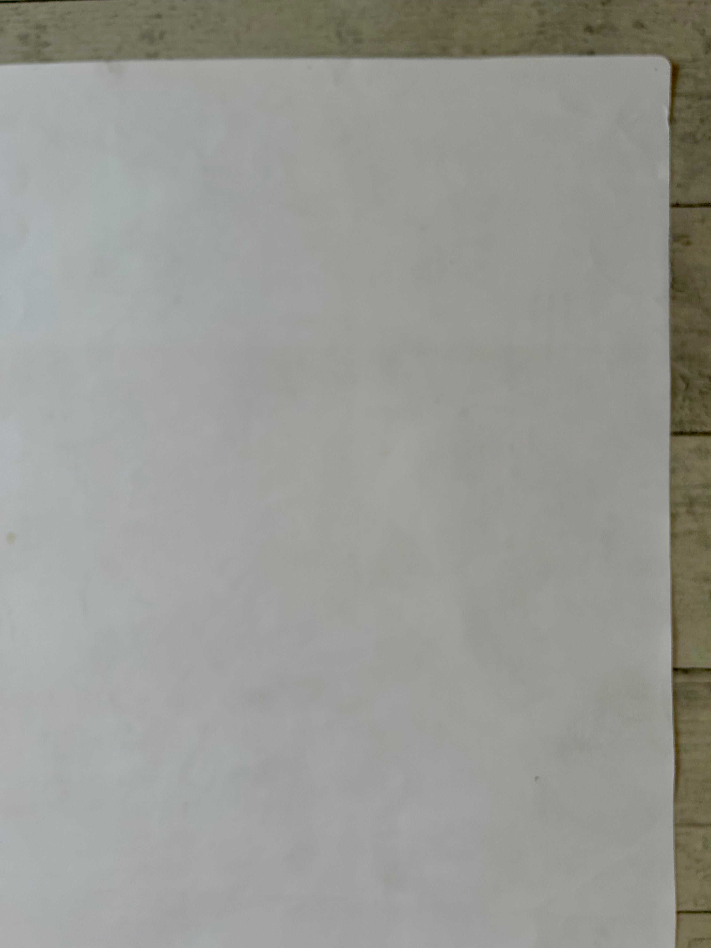 A plain white rectangular sheet or mat laid flat on a light wood surface.