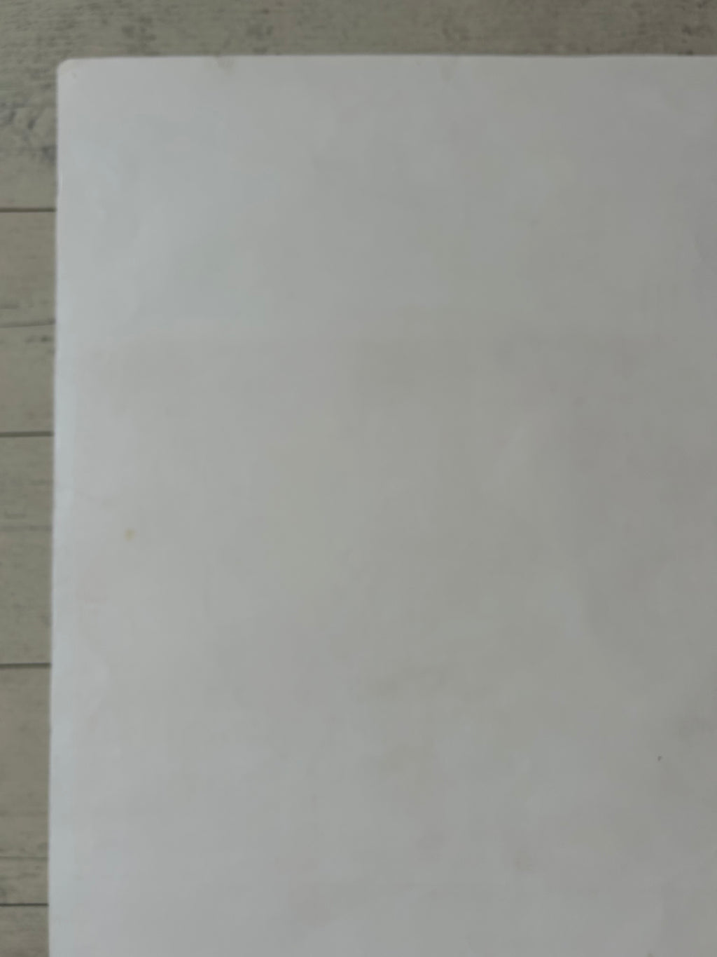 A plain white rectangular sheet or card placed on a light wood surface.