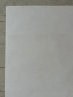 A plain white rectangular sheet or card placed on a light wood surface.