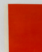 A close-up of a flat red-orange surface with a narrow off-white edge visible along the left side, photographed against a light neutral background.