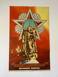 A vintage Soviet Victory poster featuring a gold-toned statue of a warrior holding a sword, set against a large silver and red star emblem with a blue central medallion. The background is a warm red and yellow gradient, with Russian text at the bottom reading 'ЗОННОТНОЕ ЯЗОЙНИЕ'.
