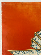 A close-up of a textured orange-red paper surface with a small decorative corner showing blue-and-white patterned paper and gold trim.