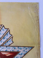 A close-up of a vintage-style printed artwork or poster showing a textured beige background with part of a geometric design in blue, brown, and red, photographed against a light wall.