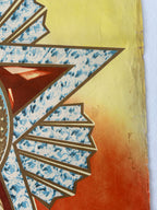 A close-up of a decorative textile or art piece featuring a stylized sunburst motif with blue marbled patterned sections, brown outlines, and a warm yellow-to-orange gradient background.