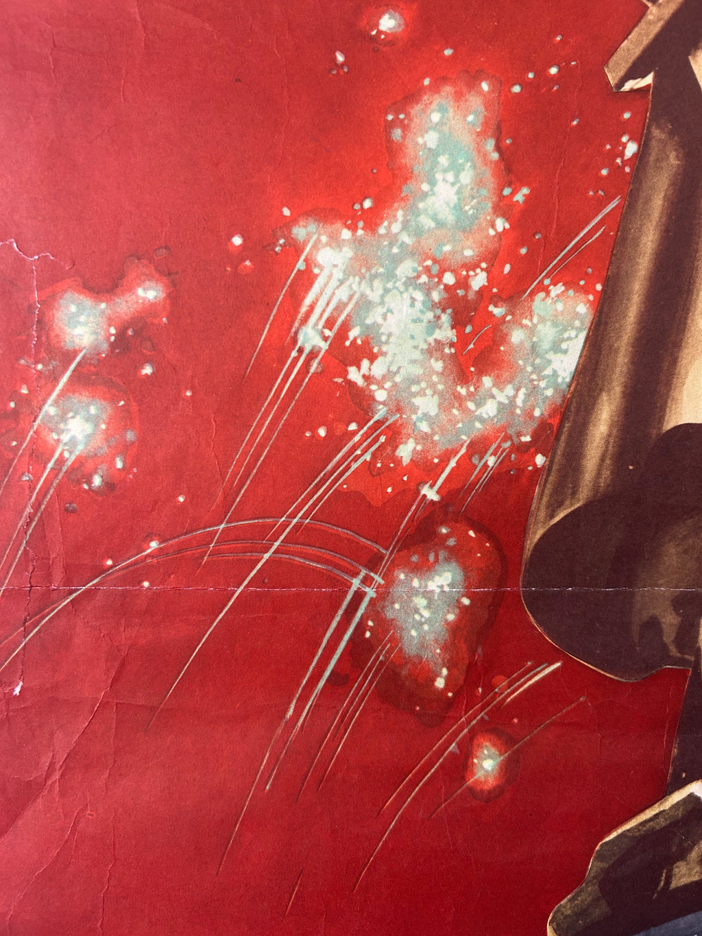 A close-up of a red printed surface with abstract white and pale blue splatter-like marks, streaks, and part of a dark brown or black object entering from the right edge.