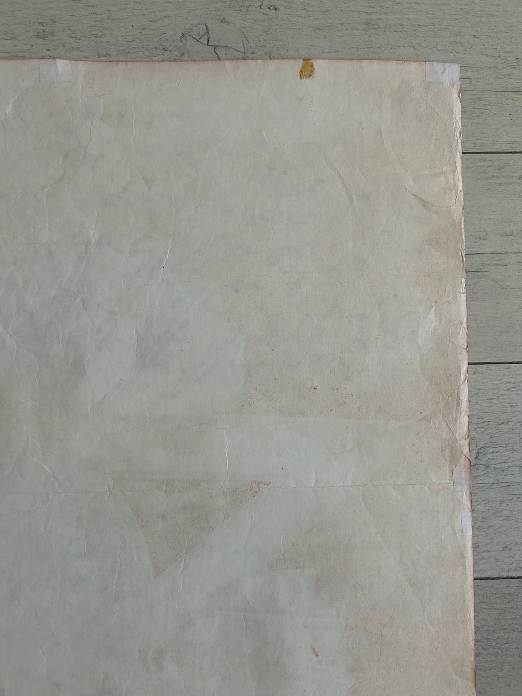 A square sheet of textured, off-white handmade paper with a warm beige undertone, laid flat on a gray wooden surface.