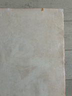 A square sheet of textured, off-white handmade paper with a warm beige undertone, laid flat on a gray wooden surface.