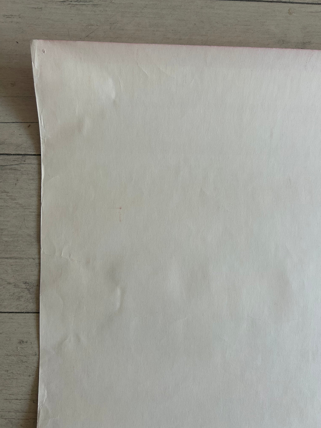 A large sheet of off-white or cream-colored paper or fabric laid flat on a light gray wood plank surface.