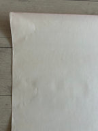 A large sheet of off-white or cream-colored paper or fabric laid flat on a light gray wood plank surface.