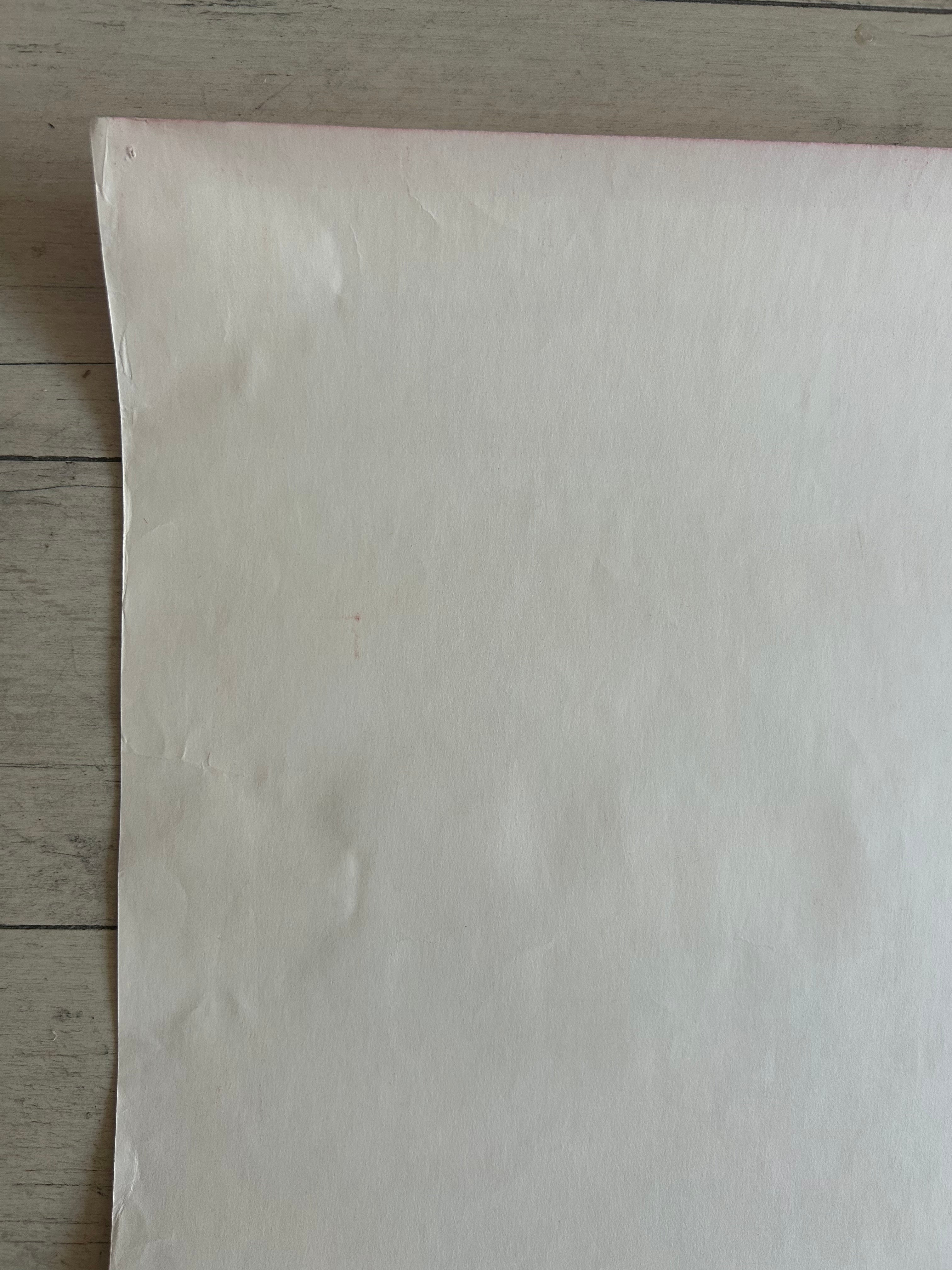 A large sheet of off-white or cream-colored paper or fabric laid flat on a light gray wood plank surface.