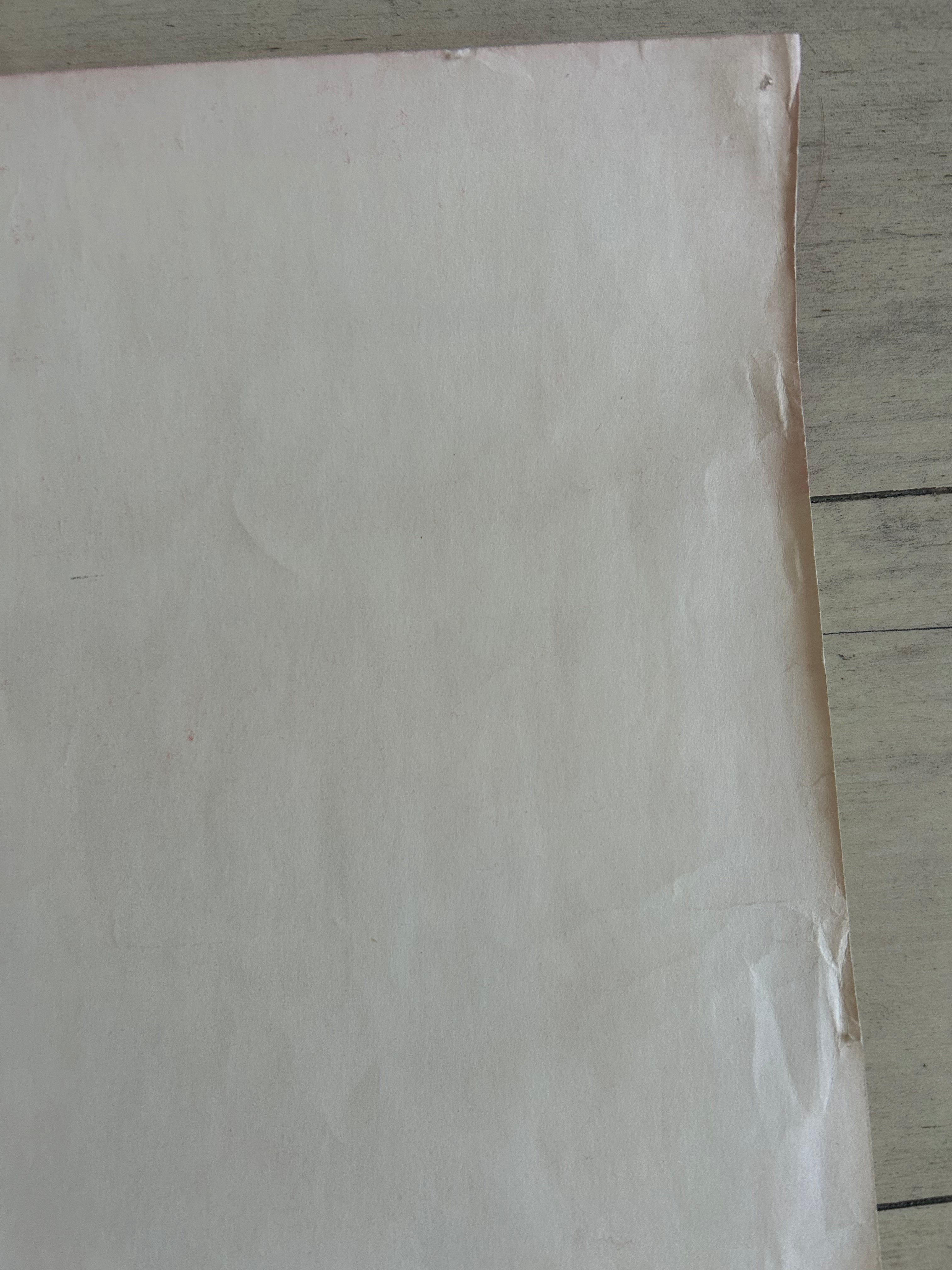 A close-up of a plain off-white sheet of paper or cardstock corner, photographed on a light wood surface.