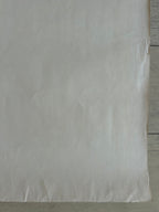 A large sheet of off-white or cream-colored paper with visible creases, laid flat on a light gray wooden surface.