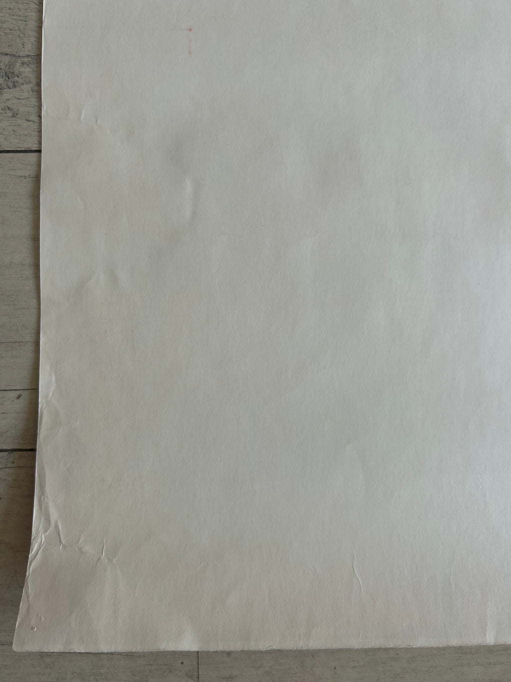 A large, blank sheet of off-white paper or cardstock laid flat on a light-colored wooden surface.