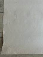 A large, blank sheet of off-white paper or cardstock laid flat on a light-colored wooden surface.