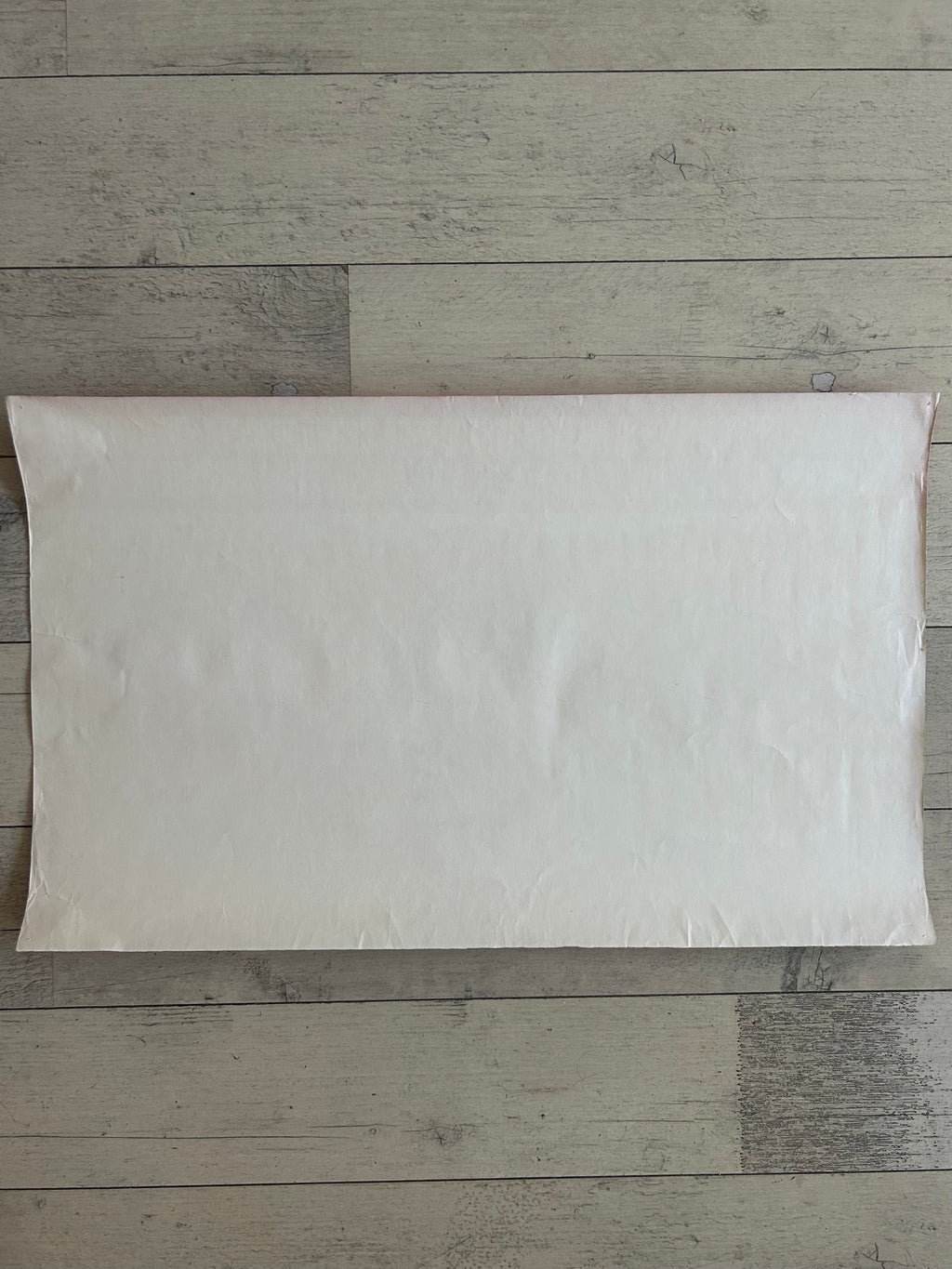 A blank, off-white rectangular pillow sham or pillow cover laid flat on a light gray wood plank floor.