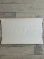 A blank, off-white rectangular pillow sham or pillow cover laid flat on a light gray wood plank floor.