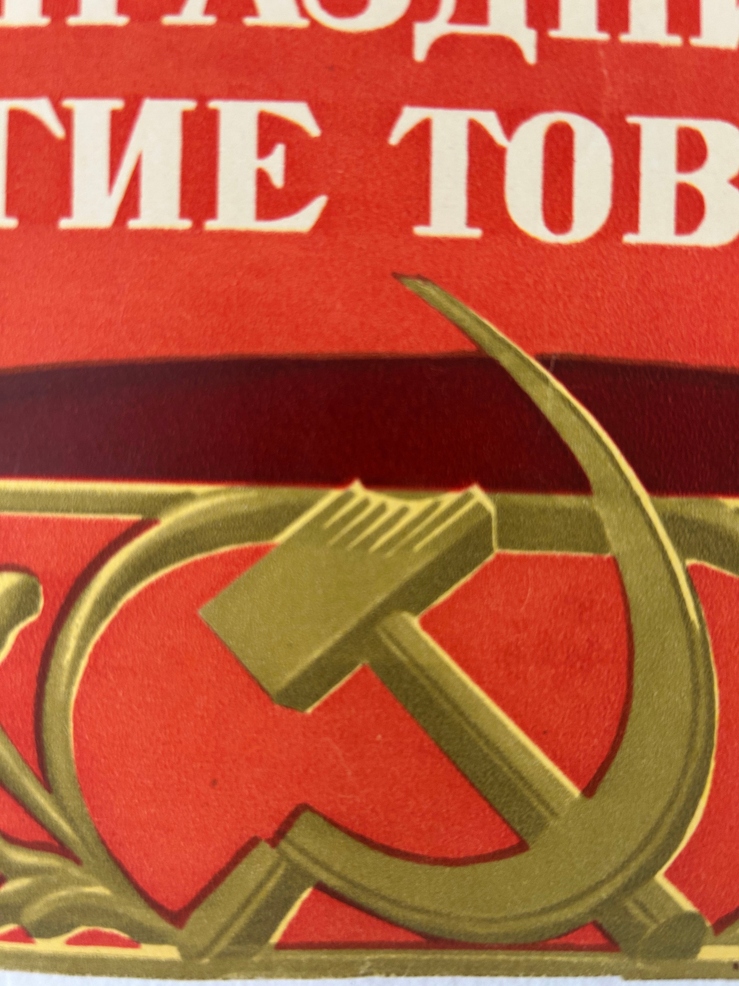 Close-up of a red Soviet-style emblem with white Cyrillic text at the top and a gold hammer and sickle motif below.