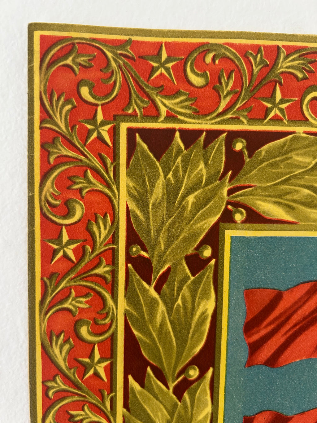 Close-up of a vintage-style decorative border with red background, gold scrollwork and stars, and gold holly leaves over a dark panel.