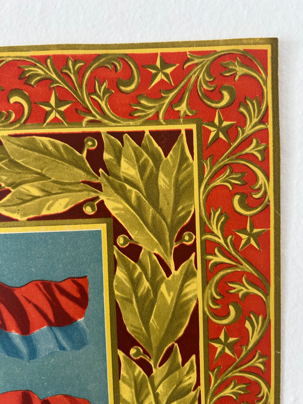Close-up of a vintage-style decorative border with red and gold ornamental scrollwork and leaf motifs, alongside a partial blue panel with red and blue graphic elements.