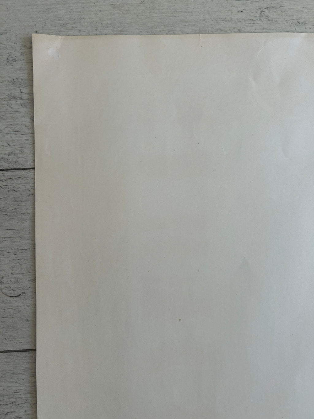 A blank, off-white sheet of paper or cardstock standing vertically on a gray wooden plank surface.