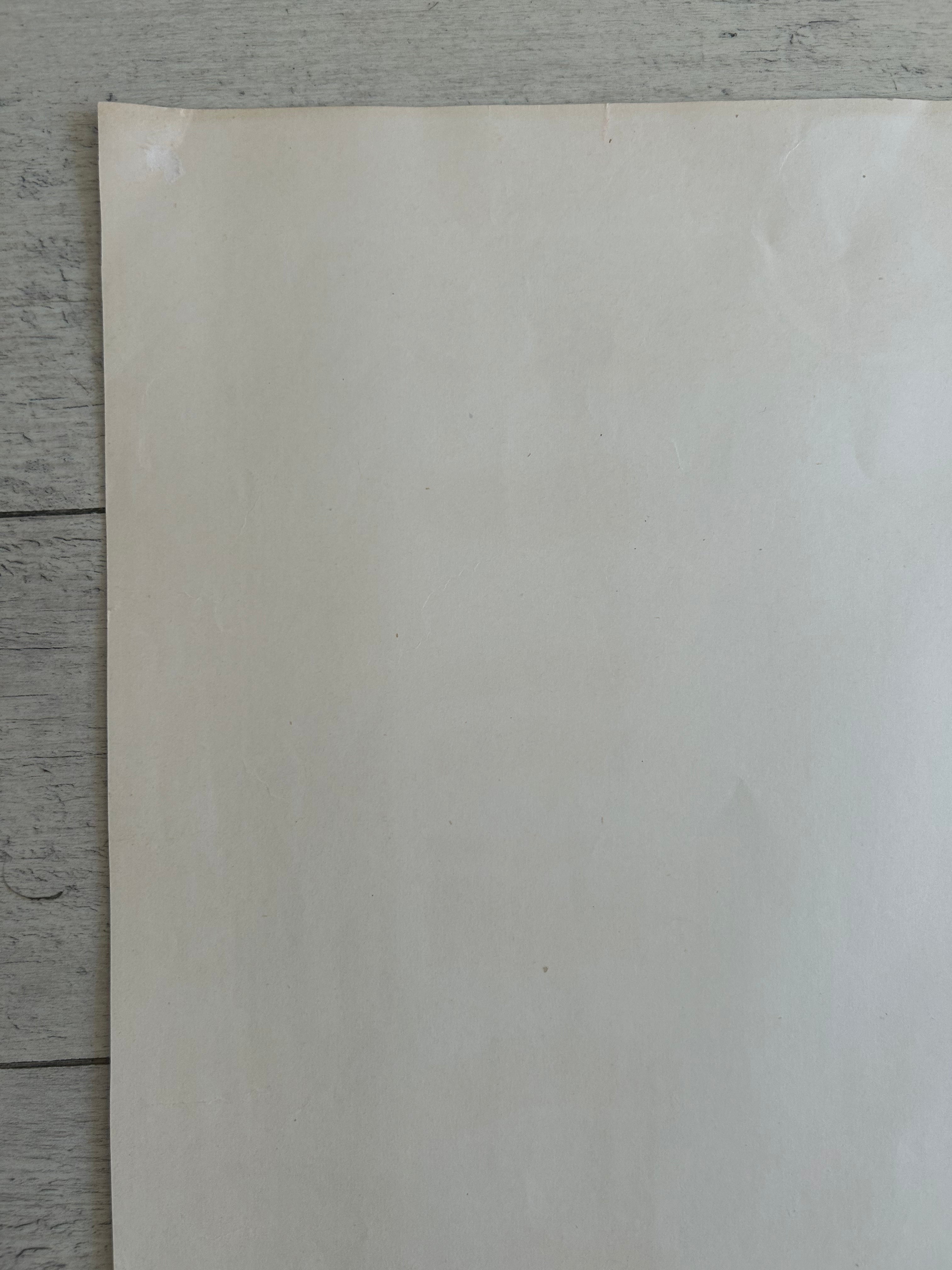 A blank, off-white sheet of paper or cardstock standing vertically on a gray wooden plank surface.