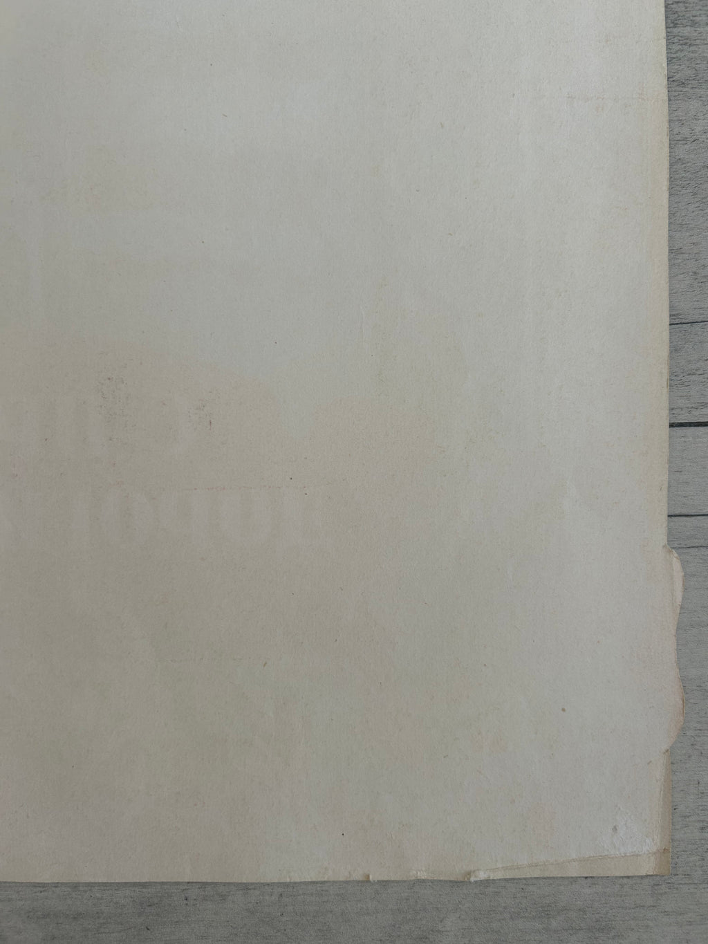 A close-up of a large beige or cream-colored sheet of paper resting on a gray wooden surface.