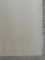 A close-up of a large beige or cream-colored sheet of paper resting on a gray wooden surface.