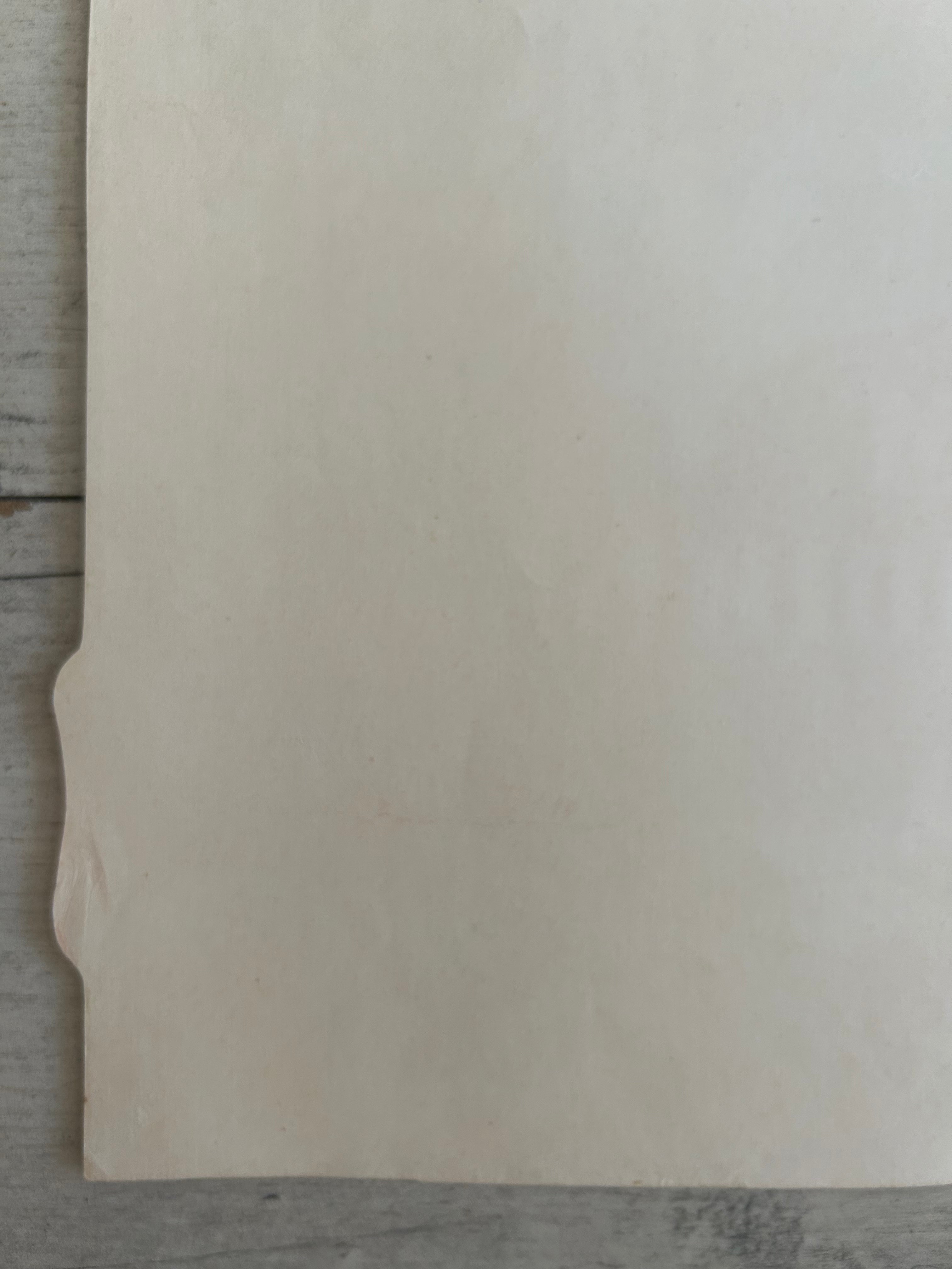 A blank, off-white sheet of paper or cardstock with a small folded tab on the left edge, resting on a gray wooden surface.