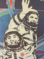 A stylized graphic print or poster showing two astronauts in white suits waving, with a dark blue background and abstract red, green, and blue shapes.