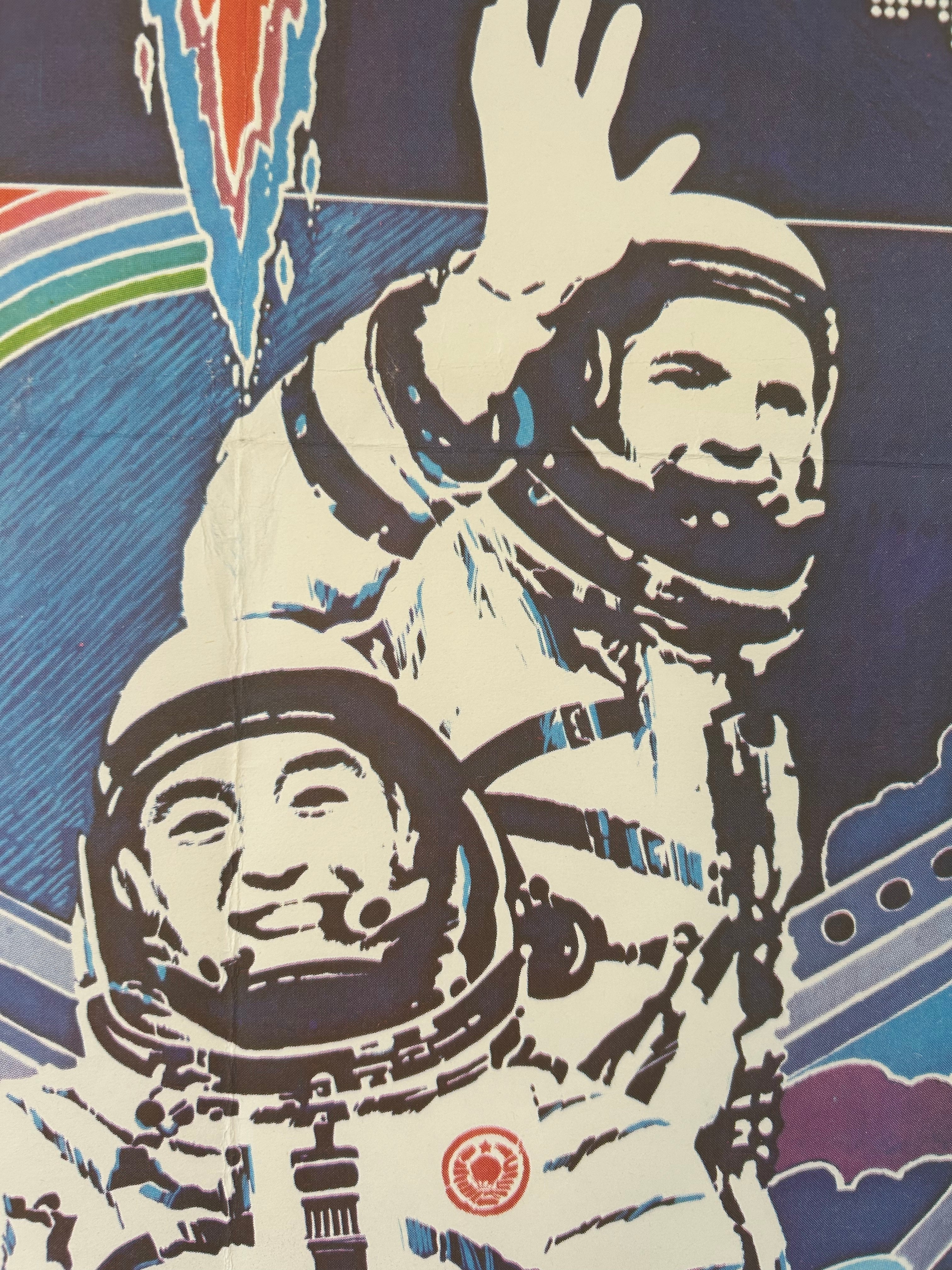 A stylized graphic print or poster showing two astronauts in white suits waving, with a dark blue background and abstract red, green, and blue shapes.