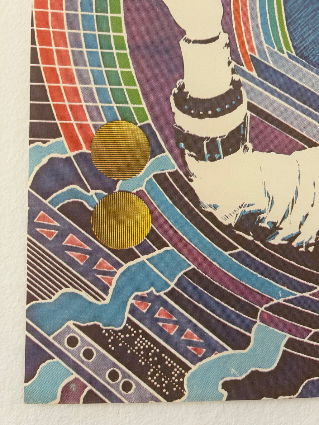 A close-up of a colorful abstract art print or poster showing a stylized hand with a bracelet, geometric patterns, blue waves, and two gold circular elements on a white textured background.