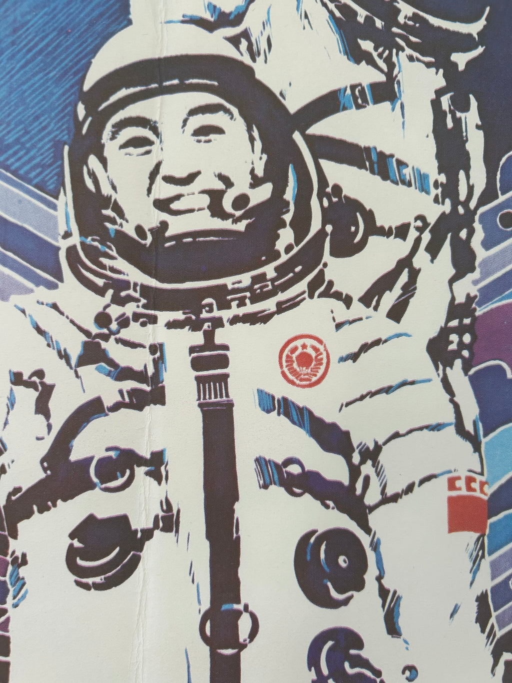 A close-up of a printed graphic featuring a stylized astronaut in a white spacesuit with bold black and blue linework, plus small red circular and square insignia on the chest and shoulder area.