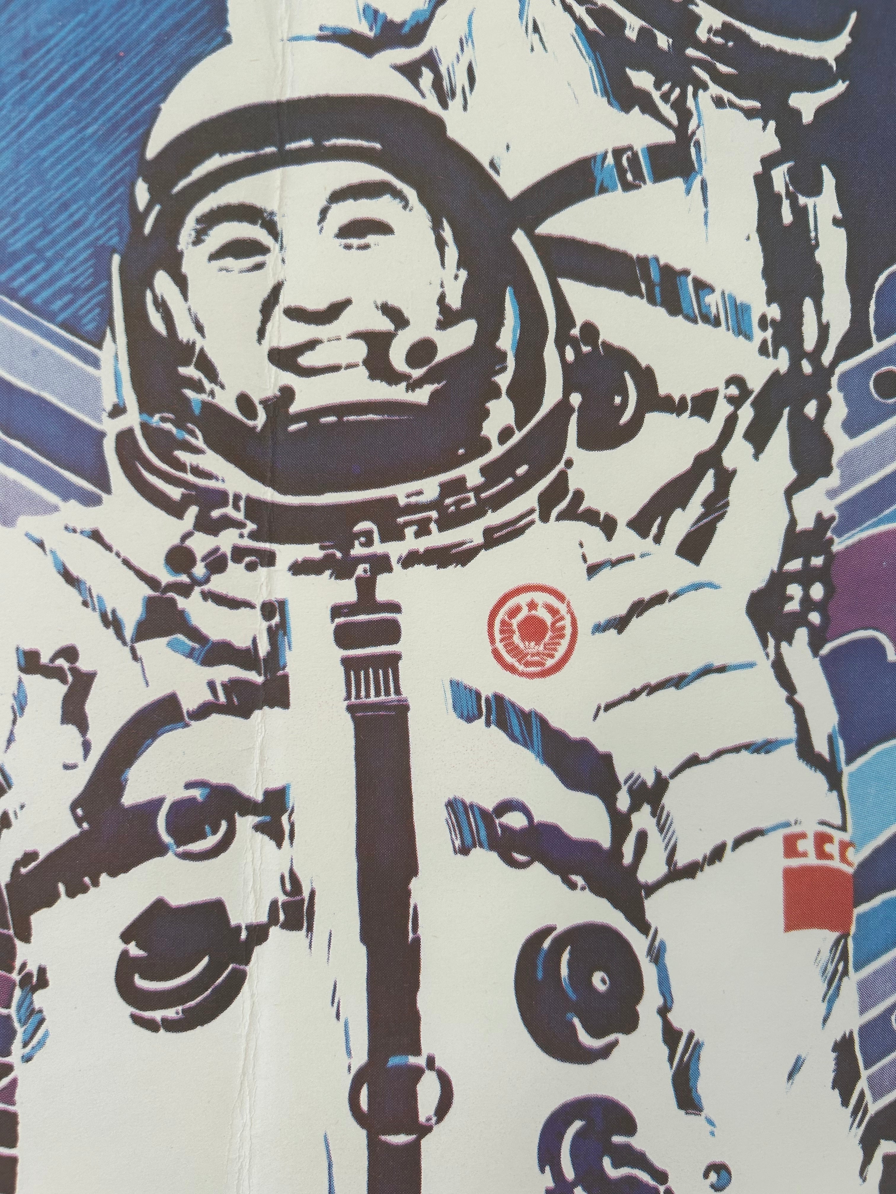 A close-up of a printed graphic featuring a stylized astronaut in a white spacesuit with bold black and blue linework, plus small red circular and square insignia on the chest and shoulder area.