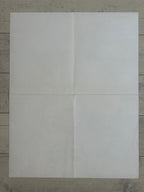A blank, off-white sheet of paper or cardstock laid flat on a gray wood-grain surface, divided by a central cross seam into four quadrants.