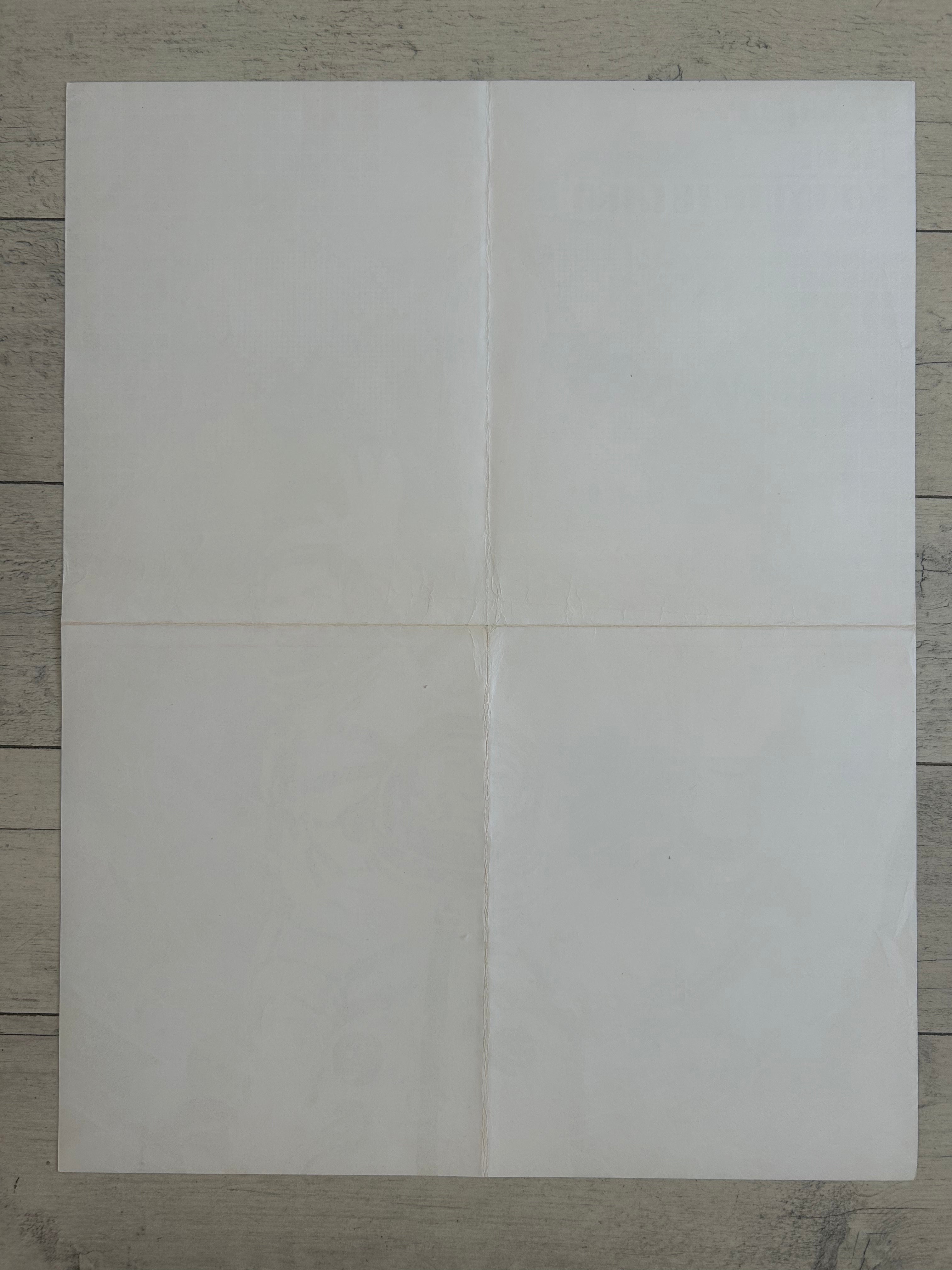 A blank, off-white sheet of paper or cardstock laid flat on a gray wood-grain surface, divided by a central cross seam into four quadrants.