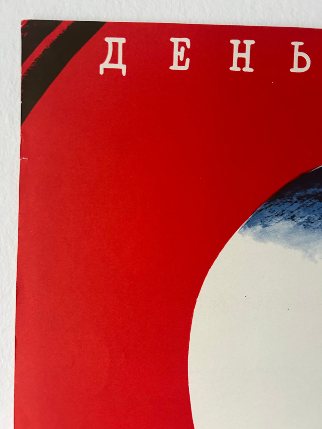 A close-up of a red printed cover or poster with white Cyrillic letters near the top and a partial blue-and-white abstract shape on the right side.
