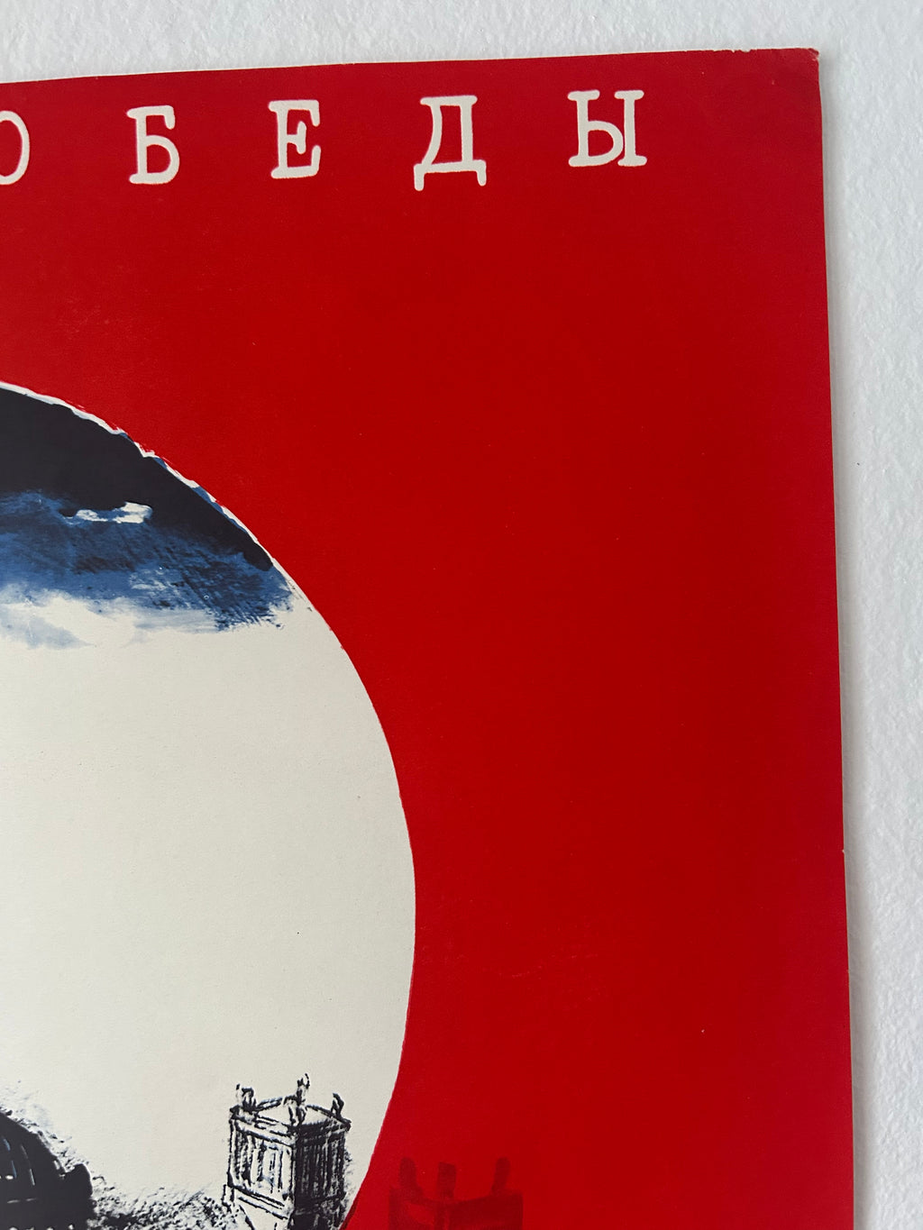 A close-up of a red poster or print featuring white Cyrillic text at the top, a large white circular shape with dark blue sky and black architectural illustration inside, and part of a white wall visible around the edges.